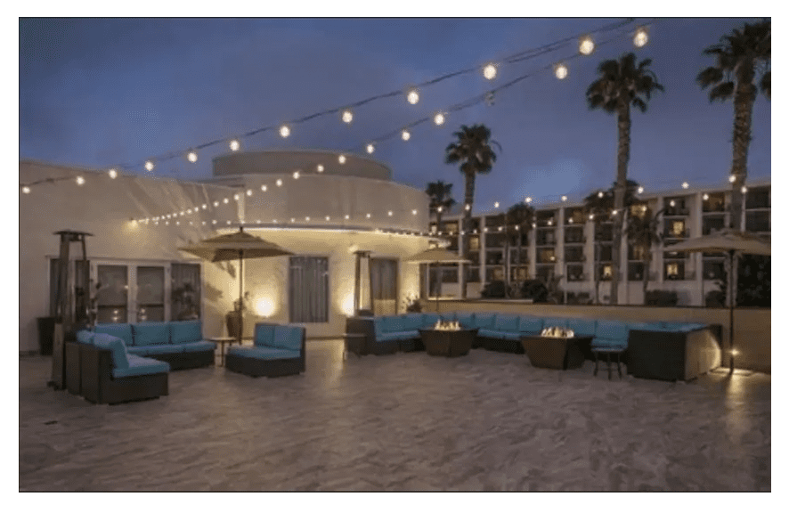 A patio with many couches and lights hanging from the ceiling.