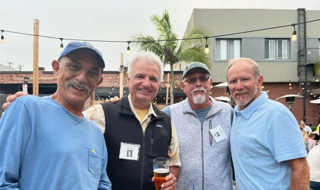 Four men standing together holding a beer.