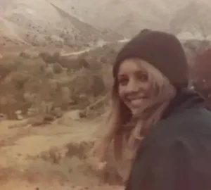 A woman in a hat and jacket standing on top of a hill.