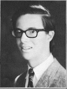 A young man wearing glasses and a suit.